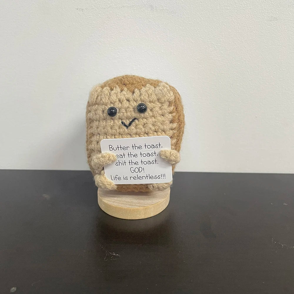 Handmade crochet toast plush doll with a sign that humorously reads "Butter the toast. Eat the toast. Shit the toast. GOD! Life is relentless!!!